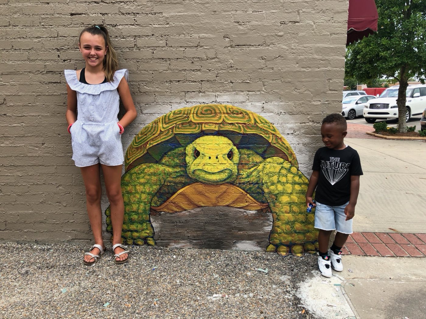 Two children beside the painted tortoise on the museum's outdoor mural