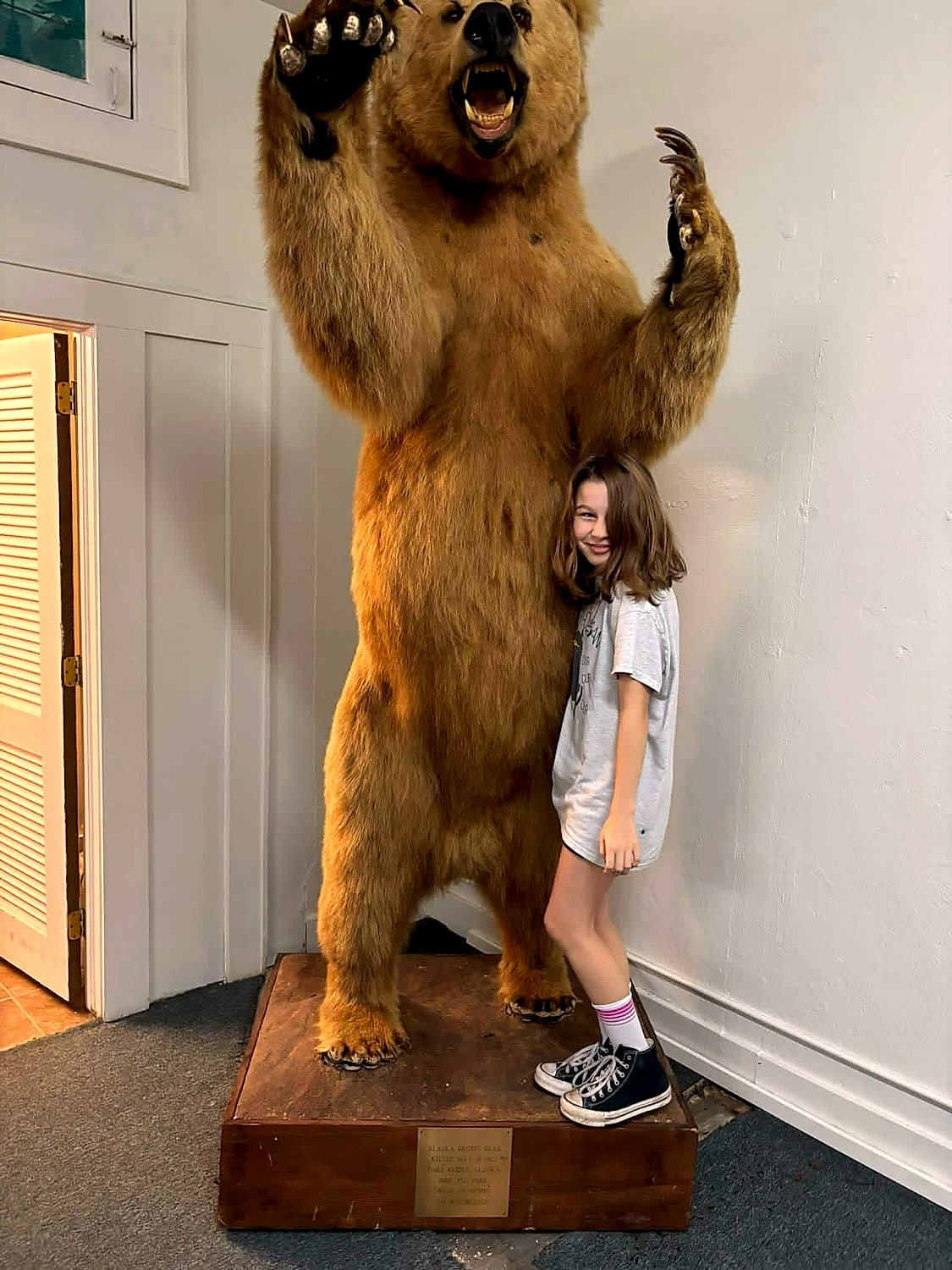 A young visitor grinning beside the museum's full-height Alaskan brown bear, reared up with claws raised